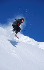 Fototapeta na wymiar Young snowboarder jumping from snow cornice and splashing snow