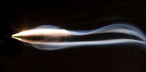 speeding bullet that has a copper jacket on a black background with smoke following behind - obrazy, fototapety, plakaty