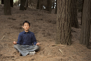 Asian boy meditating in pine forest