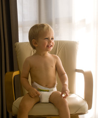 A portrait of a smiling one-year-old boy wearing only a diaper