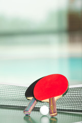 Table tennis rackets and ball, pool in the background