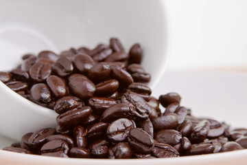 Whole dark roasted coffee beans spilling out of a cup