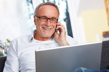 mature man with laptop mobilephone and reading specs