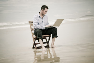 business man sitting on a chair on the beach with laptop