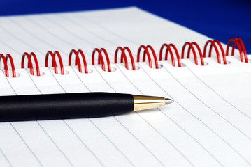Fototapeta premium The spiral note pad with a pen isolated on blue