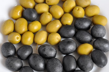 Black and green salty marinaded olives on a white plate.