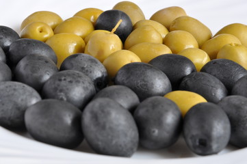 Black and green salty marinaded olives on a white plate.