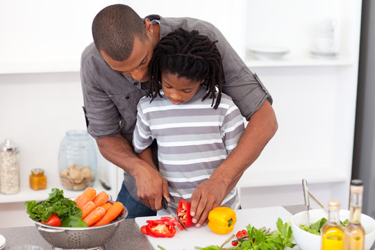 Loving afro american father helping his son cut vegetables