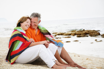 Happy mature couple sitting on the beach.