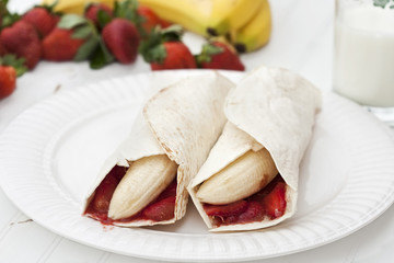 Banana and strawberry burritos on a rustic white table.