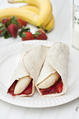 Banana and strawberry burritos on a rustic white table.