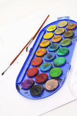 Closeup of messy, used water-color paint-box and paint brush