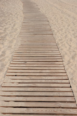 The wooden road paved by boards through a beach to the sea