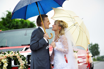 Happy bride and groom at wedding walk around red limousine