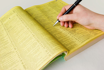 Search yellow pages with hand and pen - obrazy, fototapety, plakaty