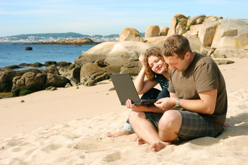 man and woman with computer at beach