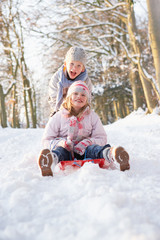 Boy And Girl Sledging Through Snowy Woodland