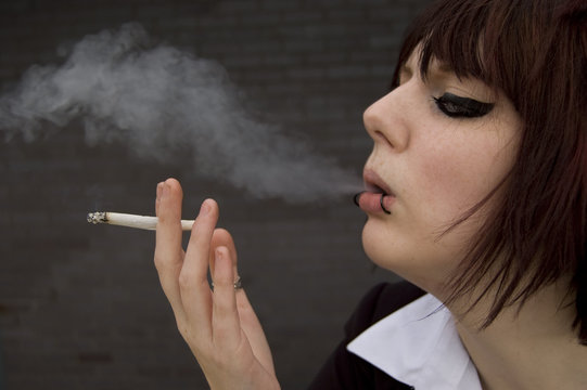 Young woman with eyeliner and piercings smokes a cigarette