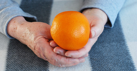 Hands of the senior woman with orange