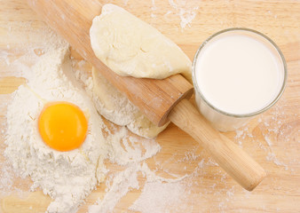 Egg yolk on flour, milk and rolling pin on wooden background