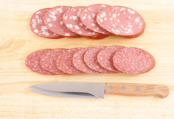 Sliced salami and knife on wooden background