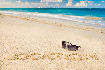 Black sun glasses on white sand beach and word vocation