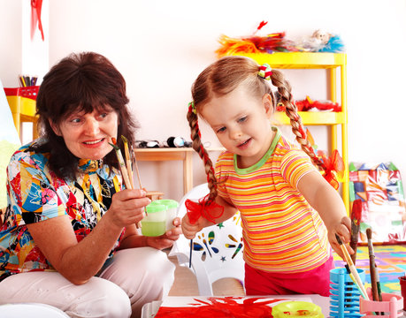 Child with teacher draw paints in playroom.