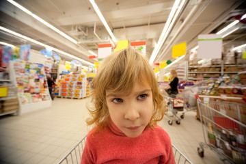 Small girl sit in shoppingcart in supermarket and look to right