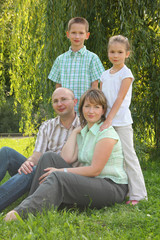 Naklejka na ściany i meble mom and dad sitting at grass. children is standing behind