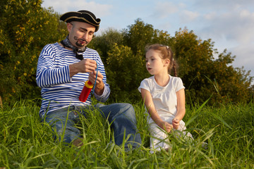 dad in pirate suit and daughter is sitting on grass.