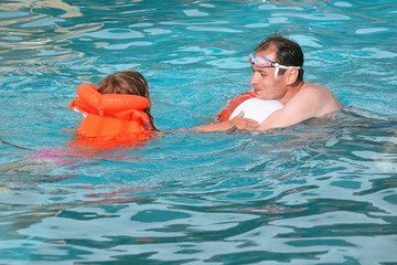 young man and little girl in lifejacket bathing  in pool