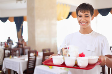 smiling affable waiter keeps tray with dishes at restaurant