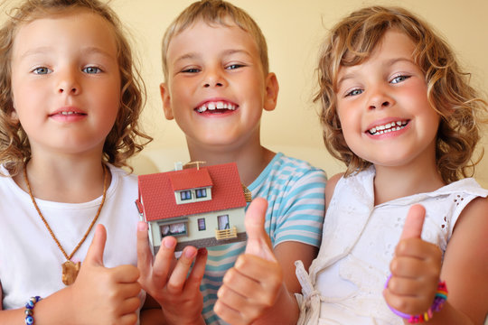 children three together keeping in hands model of house in cosy