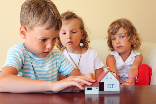 children three together looking at model of house standing