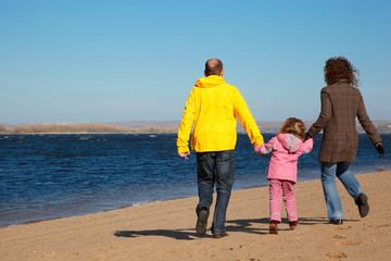 Family of three people walking along beach. View from back.