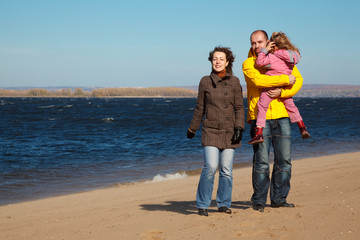 Parents with little girl walk on autumn beach.