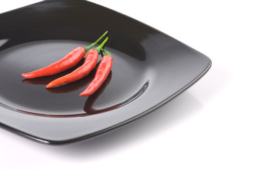 Three ripe red chili pepper on a black dish