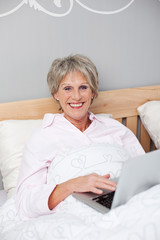 seniorin liegt im bett und surft im internet
