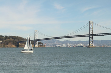 White sailboat with island and bridge as background