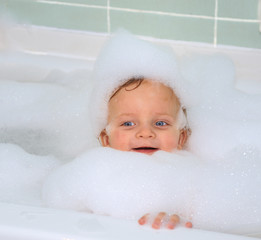 Cute little baby boy is taking a foam bath