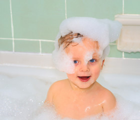 Cute little baby boy is taking a foam bath