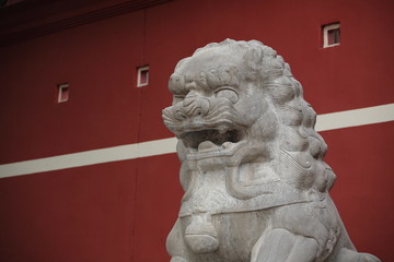 stone lion statue before the red wall.