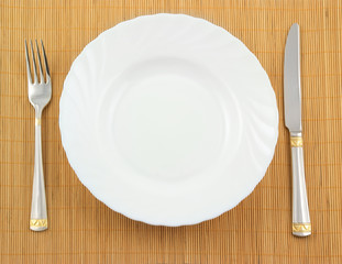 White plate, fork and knife on wooden background