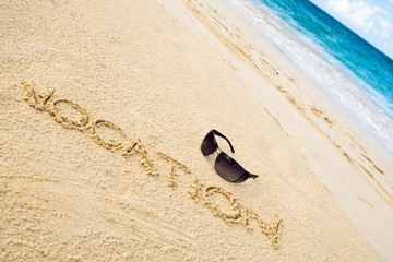 Black sun glasses on white sand beach and word vocation