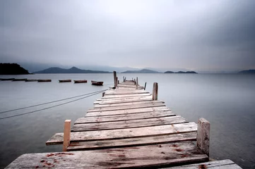 Fotobehang Kijkend over een pier en een boot, donkere toon. © leungchopan