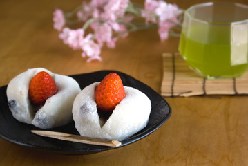 Two Japanese sweets (Ichigo Daifuku) with green tea and flowers