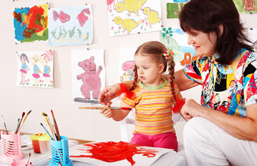Child with teacher draw paints in play room. Prescooler.