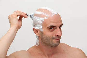 Young man shaving his head with razorblade
