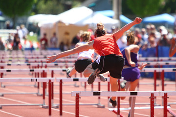 Female athletes jumping hurdles on a track.
