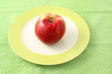 Apple in plate on a green cloth background